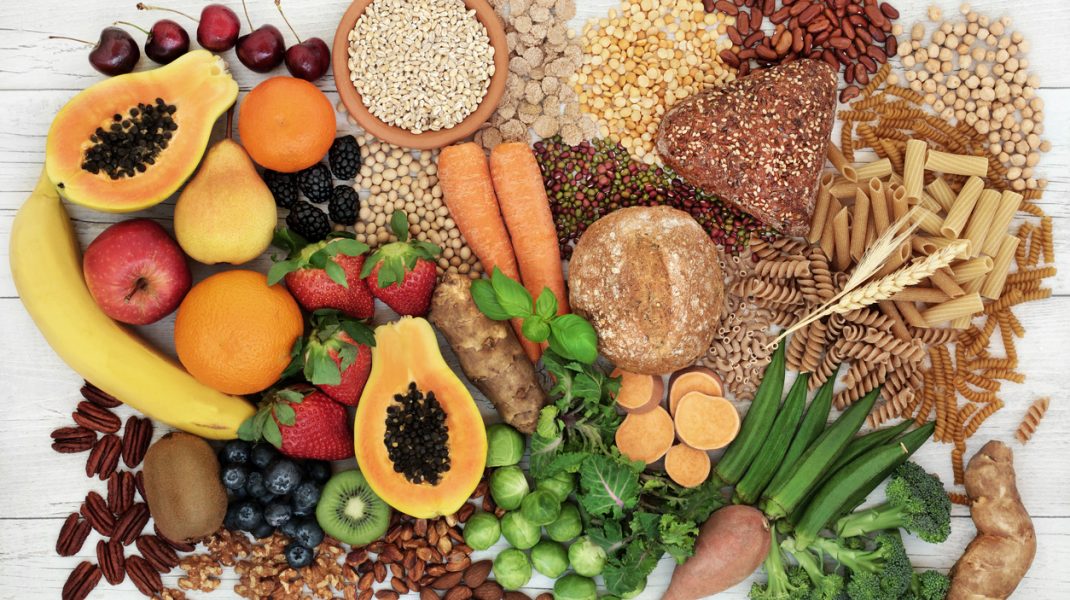 Food with high fiber content for a healthy diet with fruit, vegetables, whole wheat bread, pasta, nuts, legumes, grains and cereals. High in antioxidants, anthocyanins, vitamins and omega 3 fatty acid. Rustic background top view.