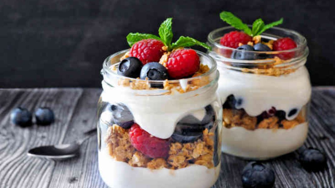 Healthy blueberry and raspberry parfaits in mason jars, scene on dark rustic background